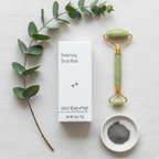 skinbetter science Detoxifying Scrub Mask white box flat lay on white linen with jade roller, ceramic dish and eucalyptus