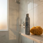 ABBA Moisture Conditioner 8 oz on light-slate stone shelf in sun-drenched modern shower with sea sponge