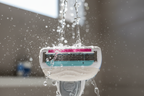Water droplets hitting white Gillette Venus Comfortglide 5-blade cartridge with pink Olay moisture bar in sunlit shower setting