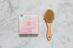 Flat lay top-down view of SOL by Jergens sunless tanning towelettes box beside exfoliating body brush