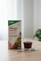Salus Floradix Floravital Liquid Iron and Vitamin Formula 500ml box on a light wood surface next to a small glass of dark red liquid supplement and a spoon in a morning wellness setting – More4less Outlet
