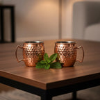 Close-up of two hammered copper shot mugs on modern wooden coffee table with fresh mint garnish in soft cocktail hour lighting