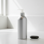 Eco-friendly silver aluminum body lotion pump bottle reflecting soft natural light in a bright minimalist spa bathroom