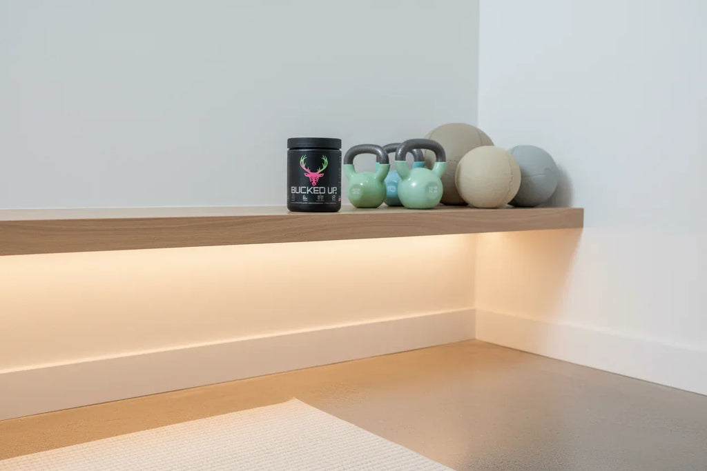 Bucked Up Pre-Workout Strawberry Kiwi on home gym shelf with kettlebells — daily fitness supplement storage