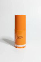 Clinical professional close-up of small orange laboratory-grade skincare serum bottle on clean white surface in bright studio lighting