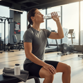 Athlete in athletic wear drinking water after gym session with white supplement bottle on workout towel