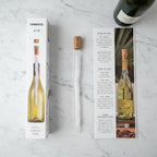 Corkcicle Air frost-tipped clear chiller device beside natural cork on white marble surface, bright studio lighting