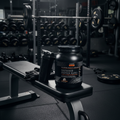 GNC AMP Sustained Protein Blend Chocolate Milkshake container on a gym bench next to a shaker bottle and workout gloves.