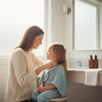 Mother carefully combing through young daughter's hair with a fine-tooth comb in a bright bathroom, warm caring moment