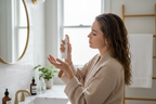 Woman applying leave-in scalp treatment spray to damp hair in bright modern bathroom hair care routine lifestyle photo