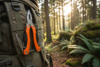 Orange handled 11-in-1 multi-tool clipped to camping backpack strap in outdoor forest setting