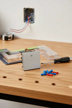 Legrand Adorne Paddle Switch package on oak workbench with precision screwdriver and wire connectors for DIY home renovation