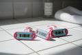 Smooth women's razor cartridges on clean white bathroom tile in soft natural lighting