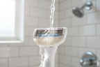 Water activating the integrated white tea moisture bar on a Gillette Venus Comfortglide razor cartridge releasing light lather in sunlit bathroom