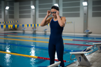 Competitive swimmer adjusting clear goggles on starting block before race, indoor pool