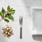 Flat lay of gel cleanser with witch hazel leaves, burdock root and white face cloth on white marble surface