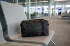 Black folding travel duffel bag on airport lounge terminal chair, modern airport interior