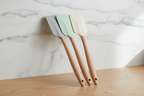Stylish silicone kitchen spatulas with wood-look handles resting on a clean wooden countertop near marble wall