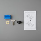 Flat-lay of all Kreg KMS7215 components: blue aluminum block, brass washer, T-bolt, black T-knob, and instruction sheet on gray workbench