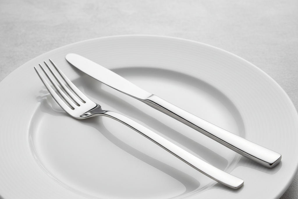 Close-up of a high-polish mirror-finish silver fork and knife on white dinnerware in soft clean studio lighting