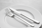 Close-up of a high-polish mirror-finish silver fork and knife on white dinnerware in soft clean studio lighting