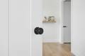 Kwikset Arroyo dummy knob matte black installed on white interior closet door in modern hallway with light wood floors - More4less Outlet