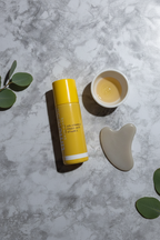 Clean lifestyle aesthetic flat lay of yellow beauty serum bottle on grey stone surface with minimal skincare accessories in soft diffused lighting