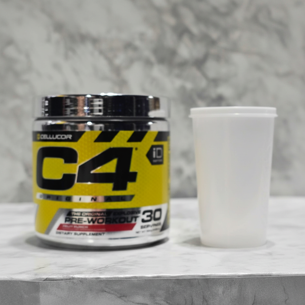 Cellucor C4 Original Fruit Punch pre-workout tub on a clean gym shelf beside a plain shaker cup