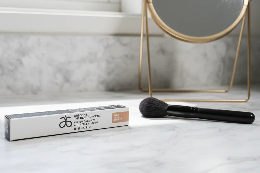 Arbonne The Real Conceal Liquid Concealer Tan on marble makeup vanity with natural daylight lifestyle