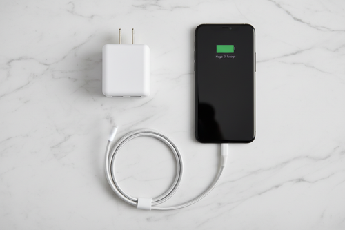 Dual-port USB wall charger next to smartphone and charging cable on white marble surface