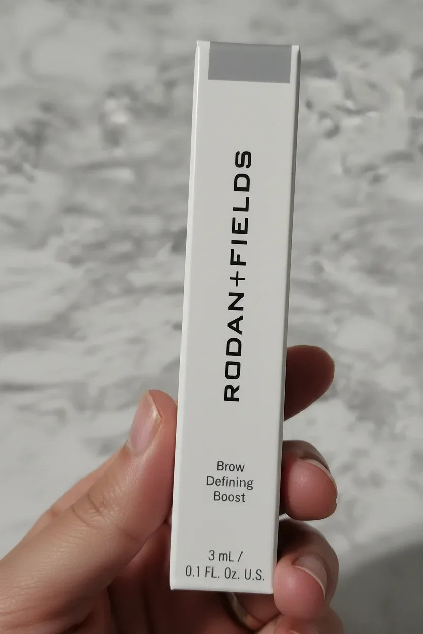 In-hand close-up of Rodan + Fields Brow Defining Boost Light retail box with macro focus on packaging text