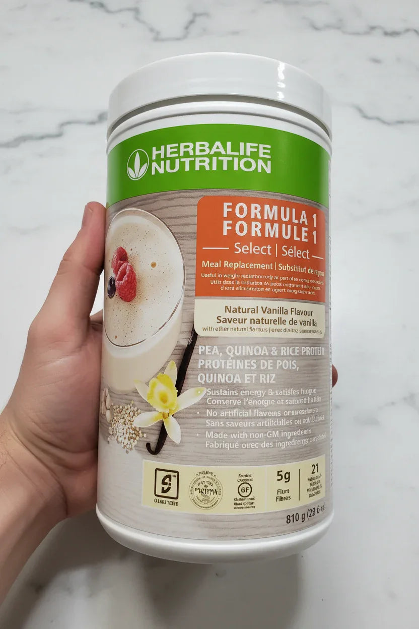 In-hand close-up of Herbalife Formula 1 Select Natural Vanilla protein supplement canister on white marble