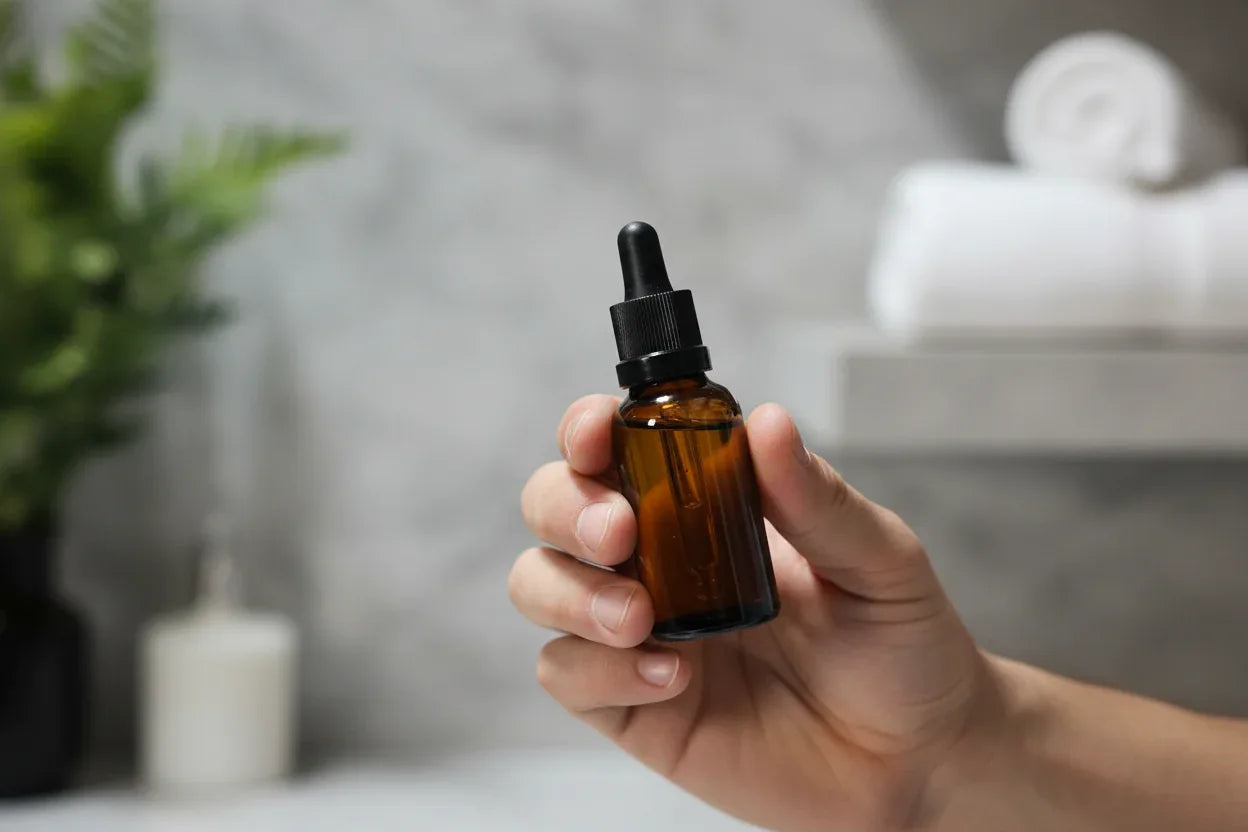 In-hand close-up of King C. Gillette dark amber glass beard oil dropper bottle with shallow depth of field