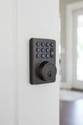 Modern oil rubbed bronze electronic deadbolt with backlit keypad installed on a clean white wooden front door