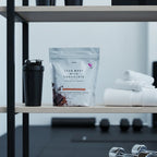 Plexus Lean Whey Milk Chocolate shake bag on minimalist home gym shelf with metal shaker cup and athletic towels