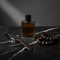Lifestyle image - dark amber cologne bottle on black marble with leather watch and wooden beads, moody editorial men's grooming flatlay for visual context only
