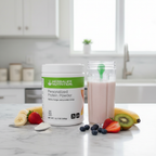White Herbalife Nutrition Personalized Protein Powder tub with green label on a marble countertop next to a blender bottle with a creamy protein shake and fresh fruit.