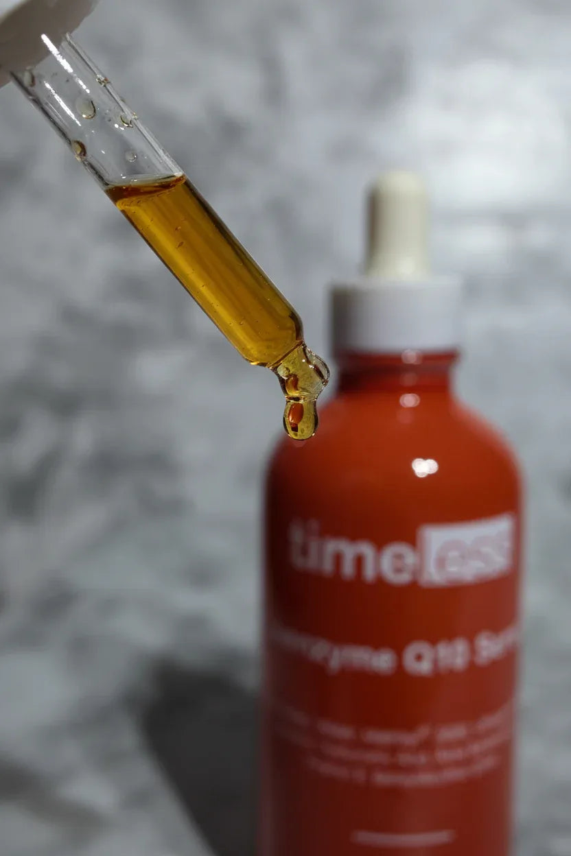 Close-up of a skincare dropper releasing a concentrated amber serum drop from a dark red-brown glass bottle in soft clean lighting