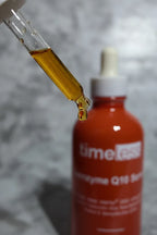 Close-up of a skincare dropper releasing a concentrated amber serum drop from a dark red-brown glass bottle in soft clean lighting