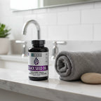 Zhou Black Seed Oil bottle on white quartz bathroom vanity shelf with rolled gray towel and decorative stone