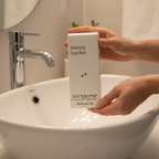 Woman holding skinbetter science Detoxifying Scrub Mask white box over a white bathroom sink during skincare routine