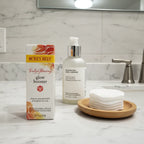 Burt's Bees Truly Glowing Glow Booster box on contemporary bathroom marble vanity next to premium facial cleanser and organic-cotton pads