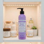 Dr. Bronner's Lavender Coconut Organic Hair Creme purple pump bottle in organized bathroom skincare cabinet shelf next to boutique glass wellness containers with soft interior lighting