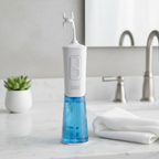 Miracle Smile Water Flosser on a marble surface next to a small succulent plant and folded white towel, minimalist spa-like bathroom setting.