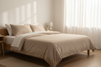 Bright airy bedroom with a king bed made up in natural tan Wellness Plus sheets, morning sunlight streaming through sheer curtains.