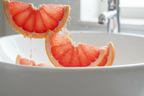 Close-up macro of fresh grapefruit slices with essential oil droplets near a clean modern white bathroom sink