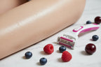 Detail of smooth hydrated skin with fresh berries and a women's razor on white marble