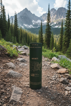 Matte dark green Akvati 32 oz stainless steel water bottle standing on a rocky trail with pine trees and mountains in the background.