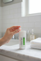 A hand applying a small amount of white mineral sunscreen to a cheek in a bright clean bathroom setting