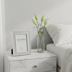 Malden silver glitter picture frame on minimalist bedroom nightstand beside white lilies, soft natural light